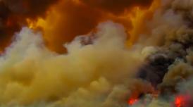 A still from Alberta Whittle's 'from the forest to the concrete'. The image is a wide angle shot of smoke billowing in huge cloud formations. In the bottom right the fire creating the smoke can be seen burning intensely.