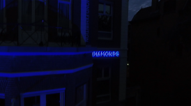 A still from Gerda Paliušytė's film. It depicts a blue neon sign on a building that says 'diamonds'