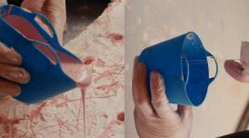 A still from the film Holly Hendry: The Art of Chaos. Gloved hands are shown pouring a pastel pink thick substance from a blue container into a textured white surface.