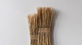 A photo of an artwork by Arko. Two bundles of Rice Straw are tastefully bound together and displayed on a blank white wall.