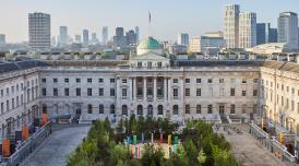 Forest for Change at Somerset House. Green leafy trees fill the courtyard. In the background you can see the London skyline and blue skies.