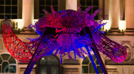 Close up of Leeroy New's installation The Arks of Gimokudan in the courtyard at Somerset House. It shows one of the sculptures, made up of reused plastic to look like a creature with arms, lit up by ambient lighting of pink, red and purple.