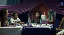 Artist Mary Sibande sitting in a textile studio talking to three women about her work