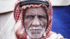 A photo of an old man wearing a head dress, looking straight into the camera, frowning slightly.