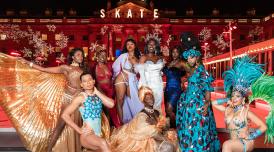 The Cocoa Butter Club pose in front of the ice rink at Somerset House. They are a group of cabaret performers, each wearing ornate, stunning gowns, feathers and sequins in bold bright colours.