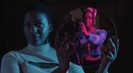 A still from the Future Producers' film Rising: A Manifesto. A Future Producer, Kayleigh, holds a circular mirror up to the camera. In the reflection you can see another Future Producer, Jahnavi, operating the camera capturing the image. 