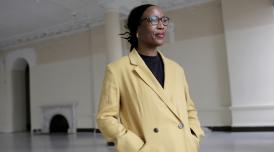A portrait photograph of the artist Sonya Dyer at Somerset House in the River Rooms, wearing a pale yellow blazer
