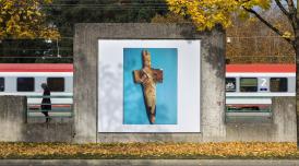 An artwork by Maeve Brennan showing a poster of a stone dagger on a blue backdrop, pasted on a concrete wall by railway tracks