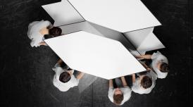 An artwork by Jasmina Cibic. An aerial view of 5 people moving a geometric, white shape across a black floor.