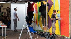 Young people handpaint a brightly coloured geometric mural on a wall.