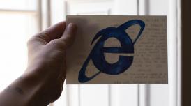A photo of a hand holding a postcard. On the front of the postcard is the letter e in blue.