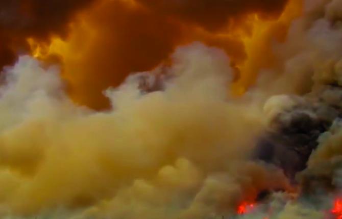 A still from Alberta Whittle's 'from the forest to the concrete'. The image is a wide angle shot of smoke billowing in huge cloud formations. In the bottom right the fire creating the smoke can be seen burning intensely.