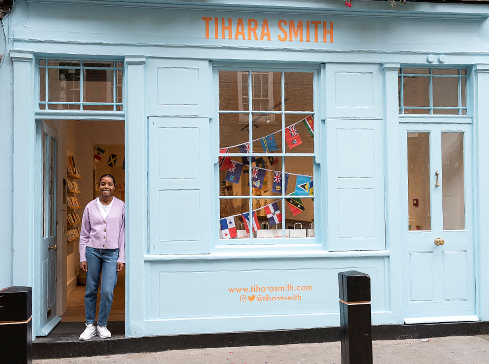 Tihara Smith, a Black woman, stands in the doorway of a blue shop, with the words Tihara Smith above the door.